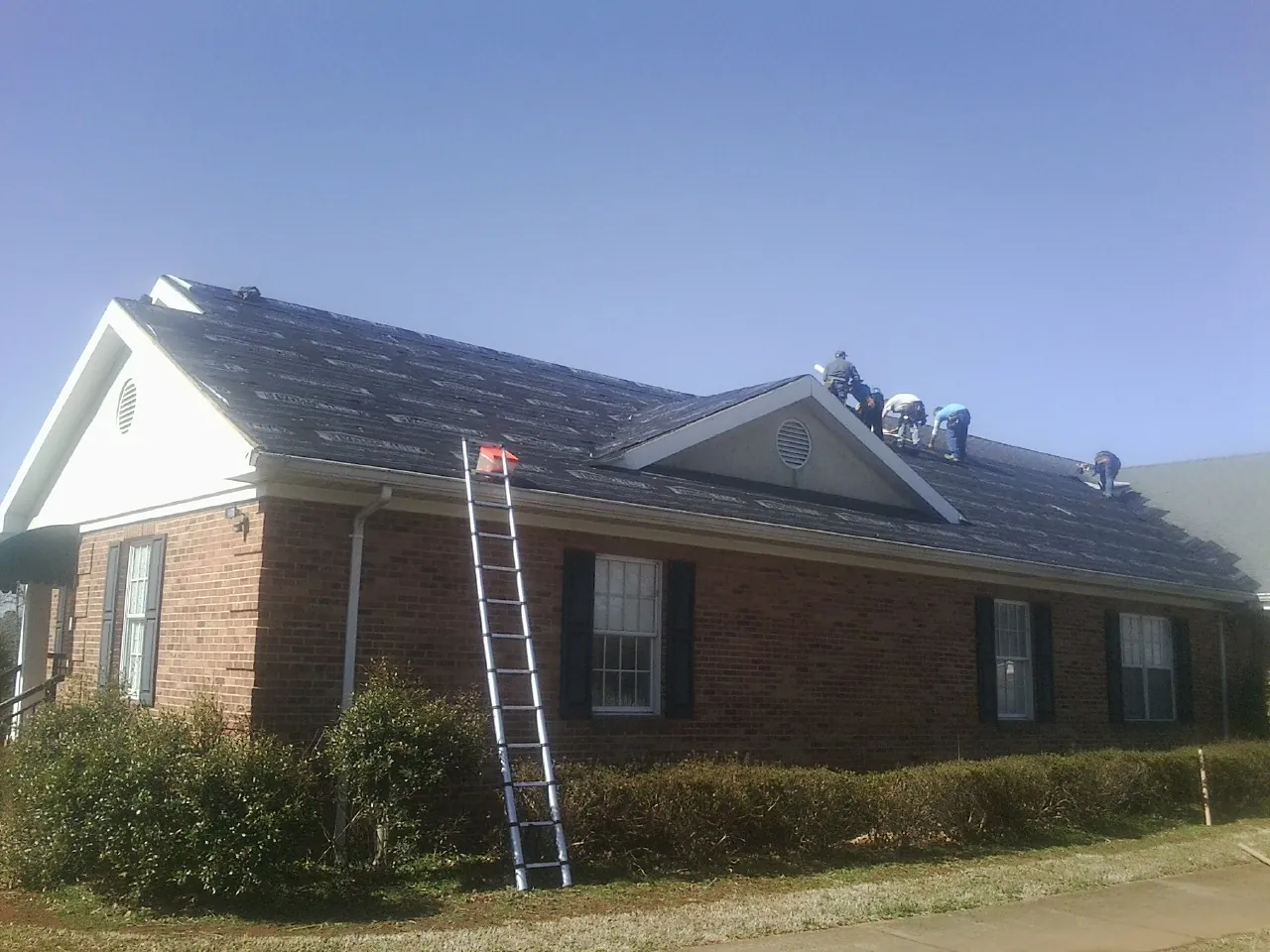 Crew tearing shingles off a brick ranch roof with a ladder set — Metal Roof Repair work by our crew in San Fernando