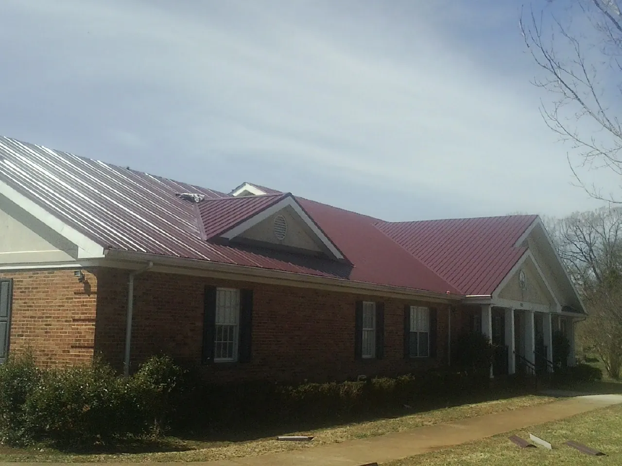 Red metal roof with gabled entries on a long brick building, from a Hail Damage Roof Repair job in San Fernando