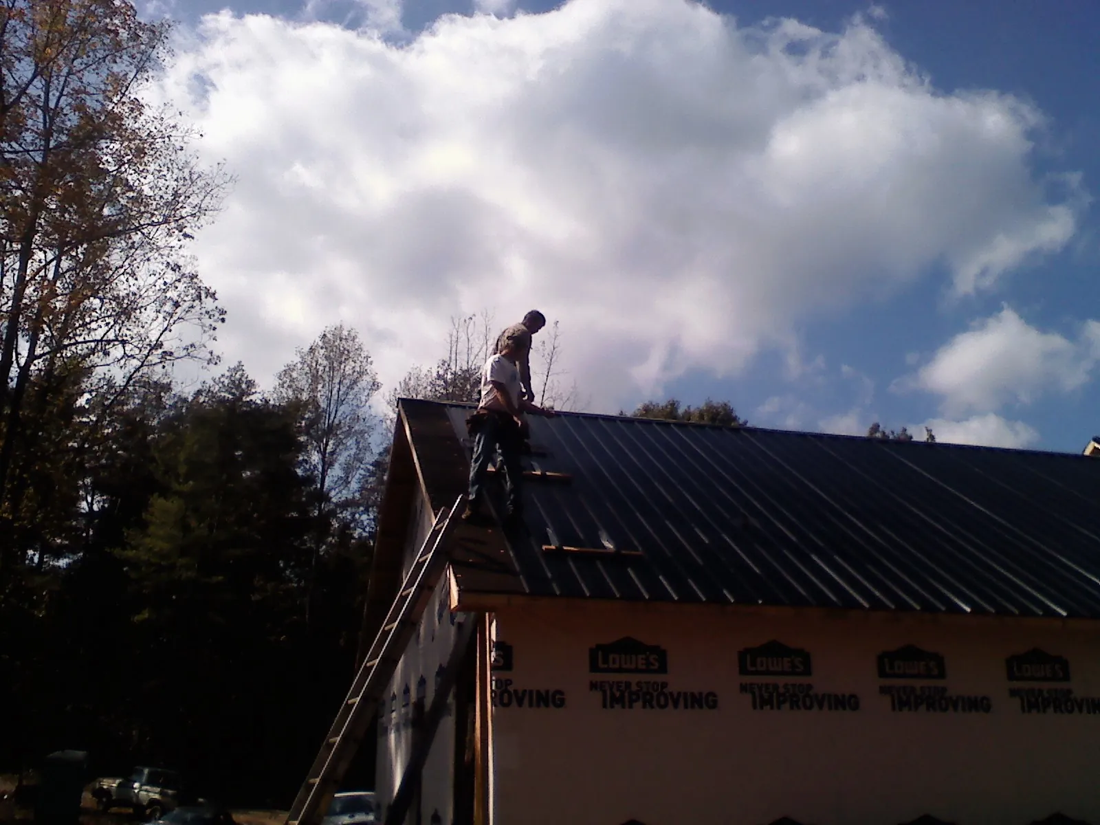 Roofer fastening dark metal panels high against a cloudy sky, from a Roof Inspection job in San Fernando