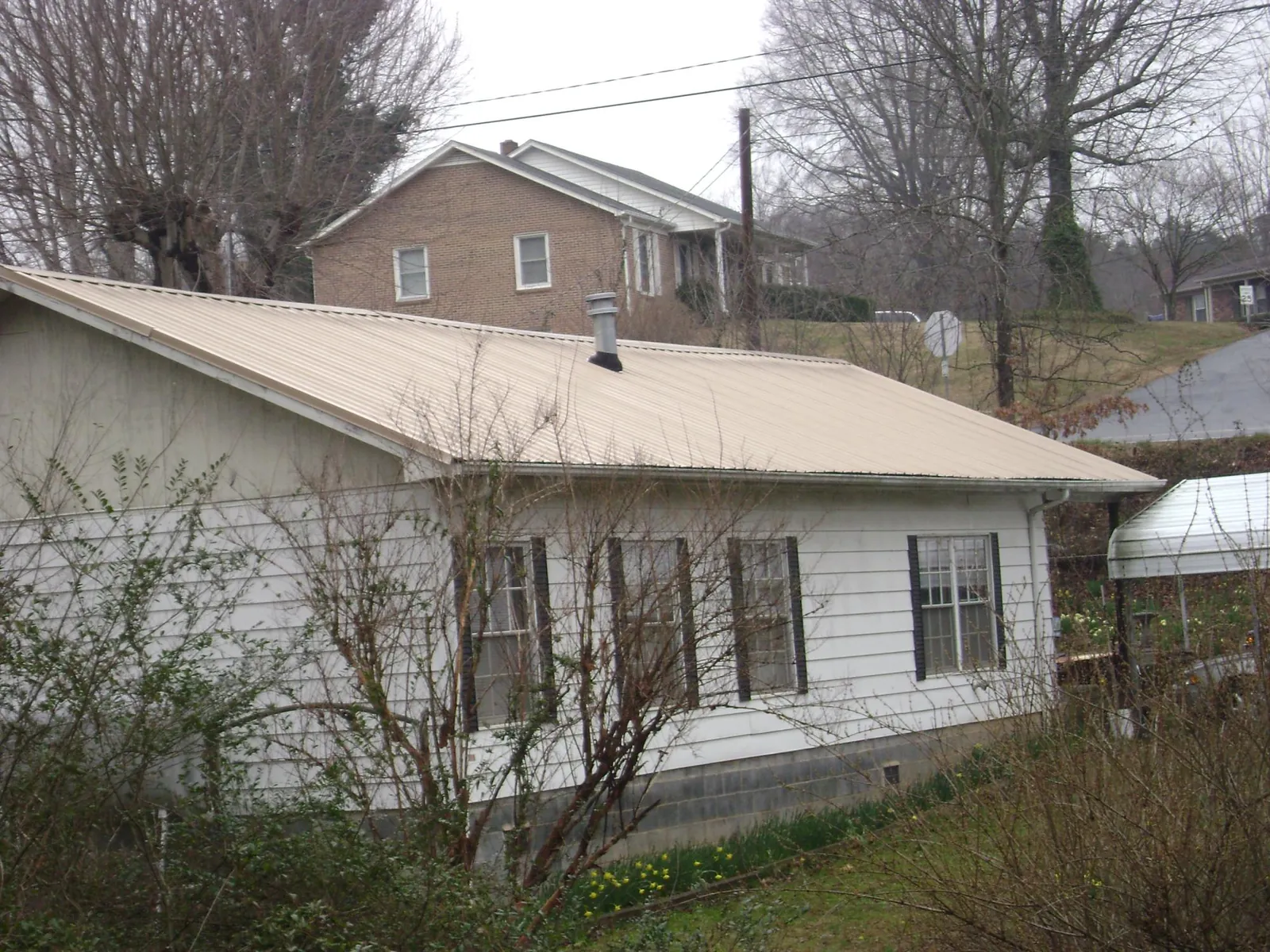 Tan metal roof on a white sided house set into a hillside — Commercial Roofing by Roofing Brothers in San Fernando